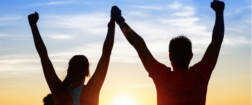 Image of two people raising their hands to the sky during a sunset