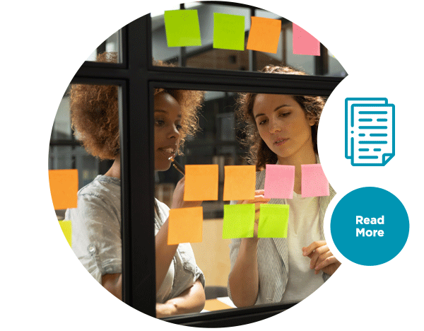 Two women looking at sticky notes attached to a glass window.